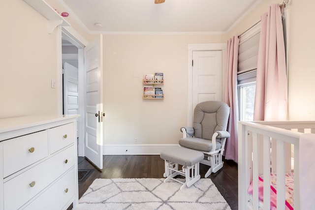 bedroom with baseboards, a nursery area, ornamental molding, and dark wood finished floors