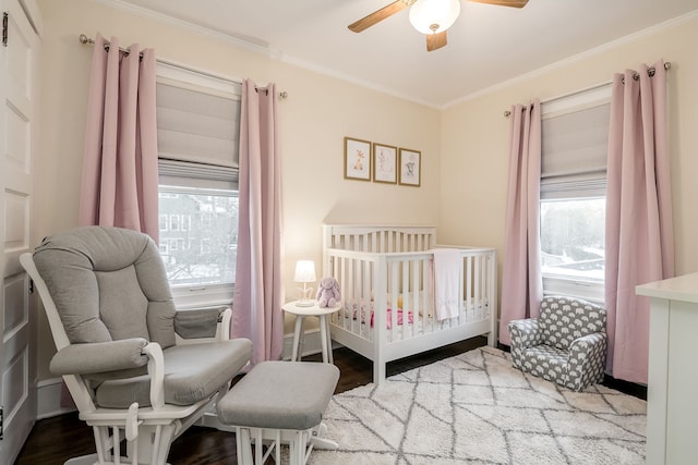 bedroom with a ceiling fan, a nursery area, wood finished floors, and crown molding