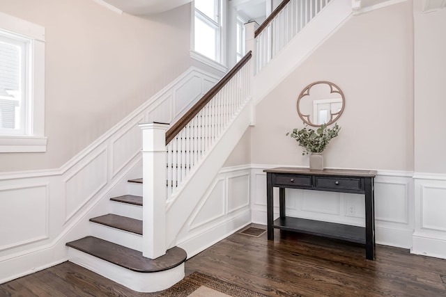 stairway with a decorative wall, wainscoting, and wood finished floors