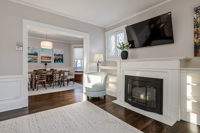 living area featuring dark wood-type flooring, a fireplace with flush hearth, crown molding, and wainscoting