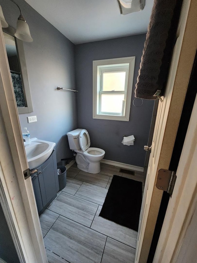 half bathroom with visible vents, toilet, vanity, and baseboards