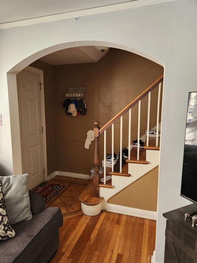 stairs with arched walkways, baseboards, and wood finished floors