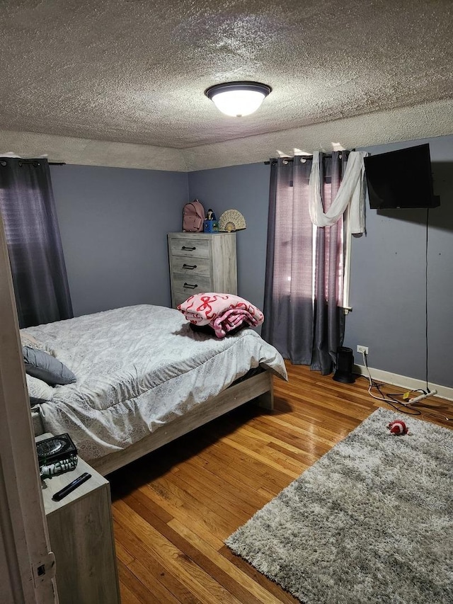 bedroom featuring wood finished floors, baseboards, and a textured ceiling