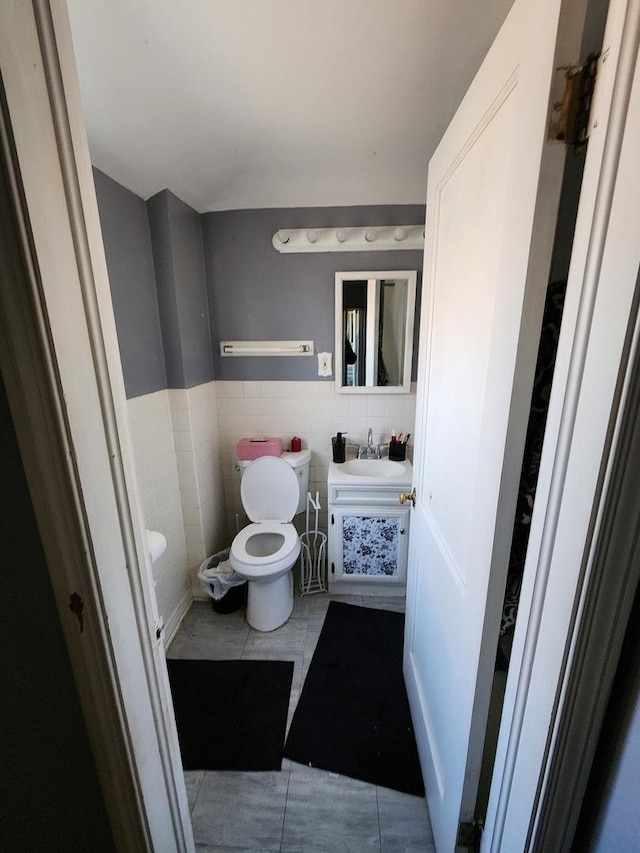 half bathroom featuring a wainscoted wall, toilet, tile walls, tile patterned flooring, and vanity