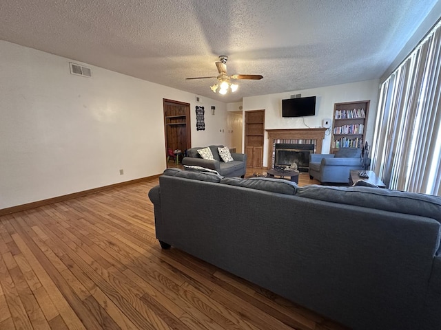 living room with a ceiling fan, baseboards, hardwood / wood-style flooring, a textured ceiling, and a glass covered fireplace