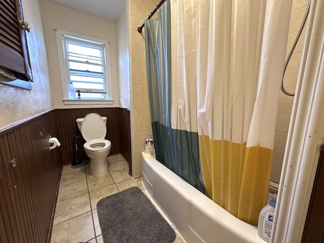 full bath featuring wooden walls, tile patterned flooring, shower / bath combo with shower curtain, wainscoting, and toilet