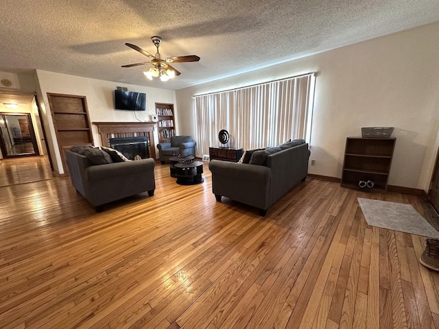 living area with a brick fireplace, baseboards, ceiling fan, hardwood / wood-style flooring, and a textured ceiling