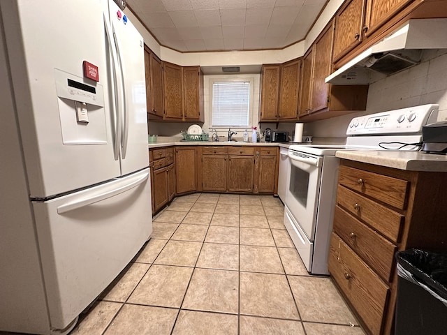 kitchen featuring brown cabinets, under cabinet range hood, white appliances, light countertops, and light tile patterned floors