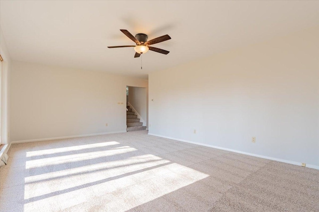 spare room featuring stairway, baseboards, light colored carpet, and ceiling fan