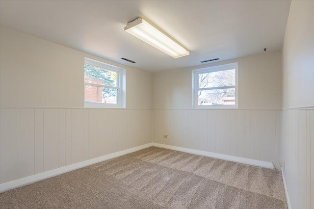 empty room with visible vents, wainscoting, and light carpet