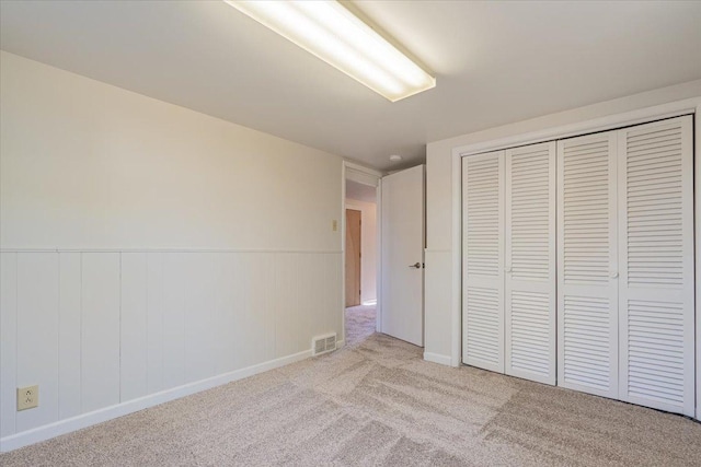 unfurnished bedroom featuring visible vents, a closet, a wainscoted wall, and carpet flooring