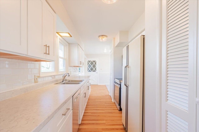 kitchen featuring a sink, dishwashing machine, white cabinetry, and freestanding refrigerator