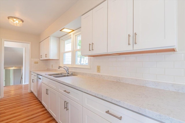 kitchen featuring a sink, backsplash, light wood-style flooring, white cabinetry, and stainless steel dishwasher