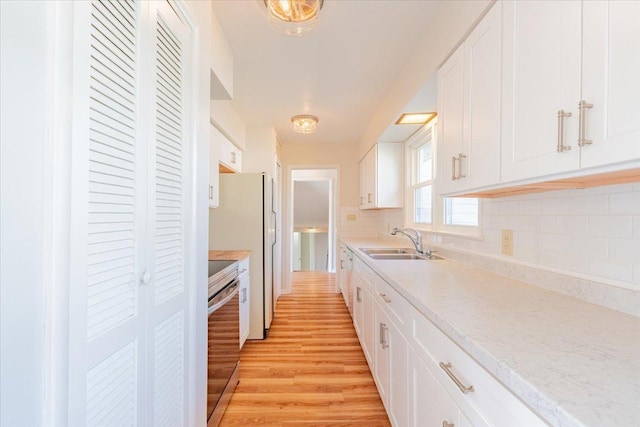 kitchen featuring tasteful backsplash, light wood-type flooring, light countertops, electric range, and a sink