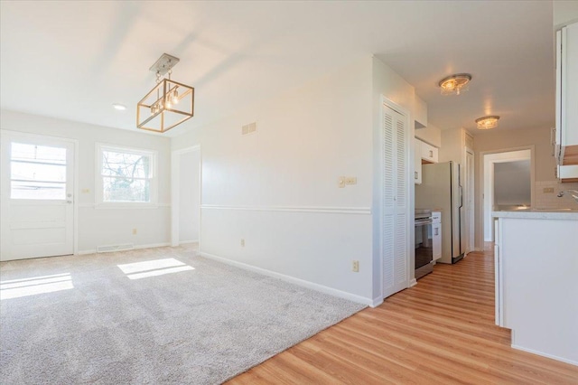 unfurnished dining area featuring light wood finished floors, visible vents, a chandelier, and baseboards