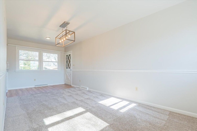 spare room featuring visible vents, carpet floors, a notable chandelier, and baseboards