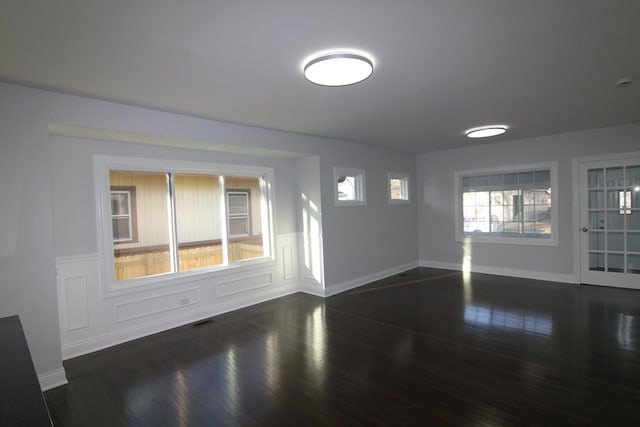 spare room with dark wood-type flooring, a decorative wall, baseboards, and visible vents