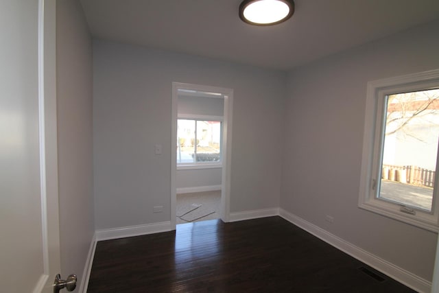 unfurnished room featuring visible vents, dark wood-style floors, and baseboards