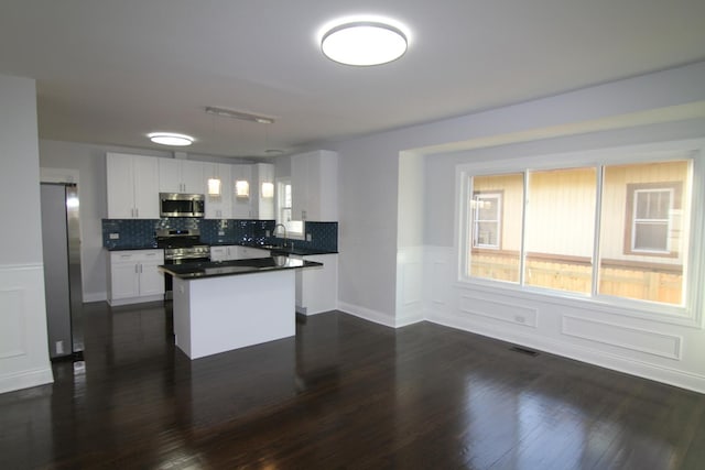 kitchen featuring visible vents, a kitchen island, dark wood finished floors, stainless steel appliances, and white cabinetry