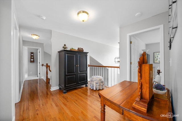 corridor with light wood-type flooring, an upstairs landing, and baseboards