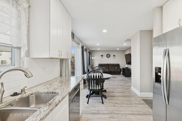 kitchen featuring backsplash, light wood-type flooring, white cabinets, stainless steel appliances, and a sink