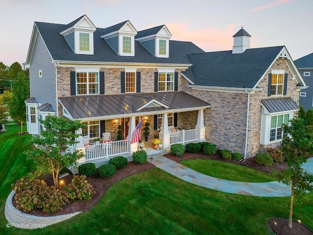 view of front of property with a porch, a lawn, and stone siding