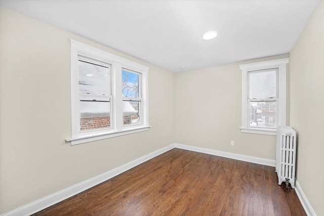 spare room featuring dark wood finished floors, radiator heating unit, and baseboards