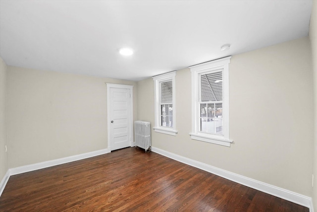 empty room featuring baseboards, dark wood-style flooring, and radiator heating unit