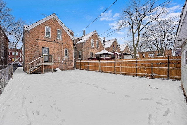 snow covered back of property with brick siding and a fenced backyard