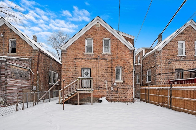 snow covered house featuring fence and brick siding