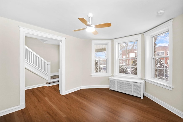 empty room with baseboards, radiator, wood finished floors, and stairs