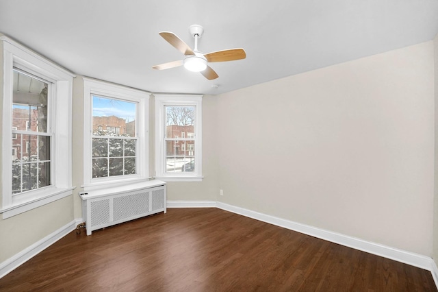 empty room featuring dark wood-style floors, ceiling fan, radiator heating unit, and baseboards