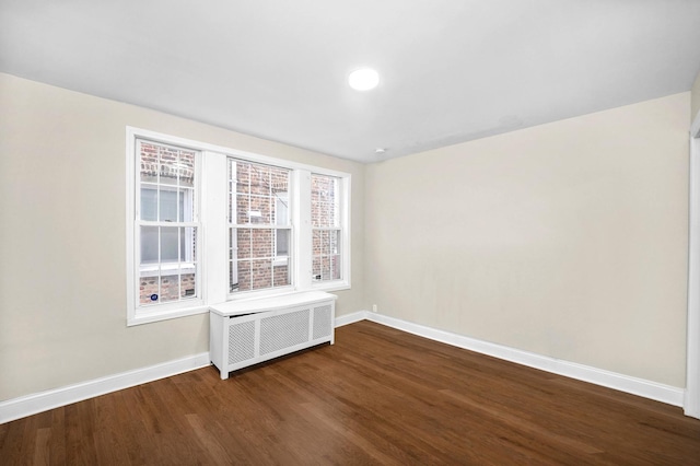 spare room with baseboards, dark wood-style floors, and radiator heating unit