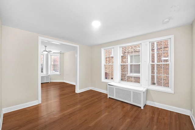 unfurnished room with radiator heating unit, wood finished floors, and baseboards