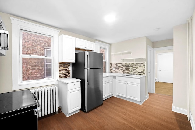 kitchen with light countertops, radiator heating unit, light wood-style flooring, freestanding refrigerator, and a sink