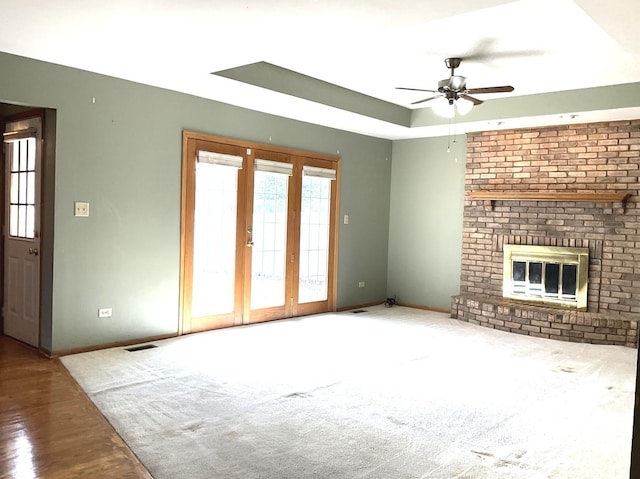 unfurnished living room with baseboards, visible vents, a tray ceiling, a fireplace, and ceiling fan