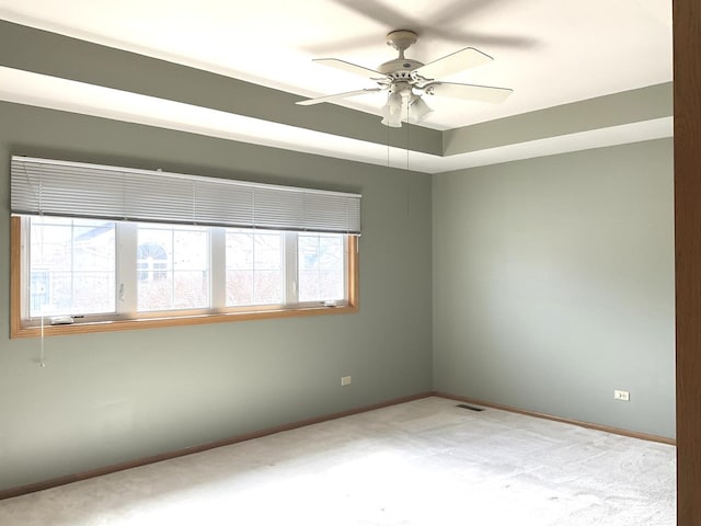 carpeted empty room with a tray ceiling, visible vents, baseboards, and a ceiling fan