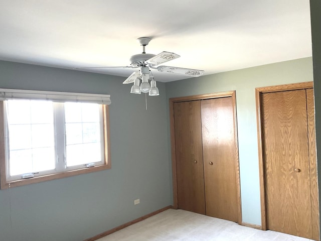 unfurnished bedroom featuring light colored carpet, baseboards, two closets, and ceiling fan