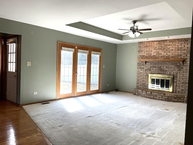 unfurnished living room with baseboards, a tray ceiling, ceiling fan, a brick fireplace, and carpet flooring