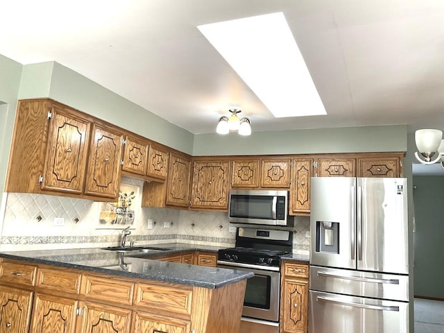 kitchen featuring brown cabinetry, a skylight, a sink, decorative backsplash, and stainless steel appliances