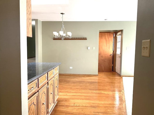 kitchen featuring dark stone counters, light wood-style floors, a chandelier, and hanging light fixtures