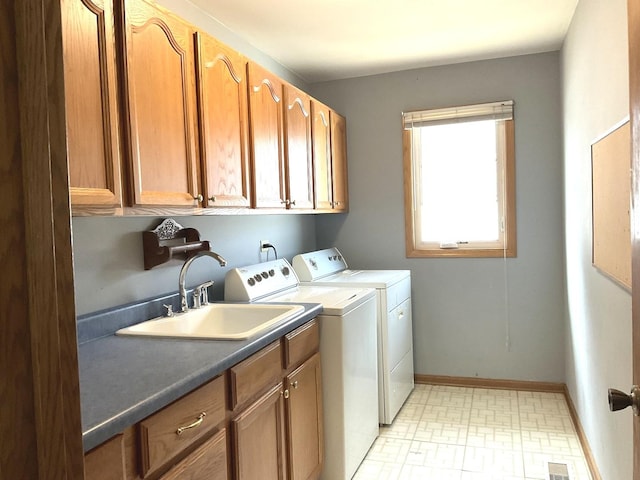 washroom with visible vents, a sink, washing machine and dryer, cabinet space, and baseboards