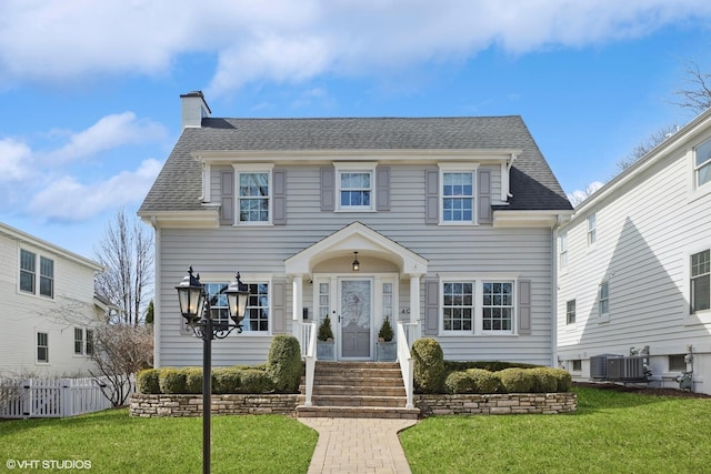 colonial inspired home featuring a front lawn, fence, roof with shingles, and a chimney