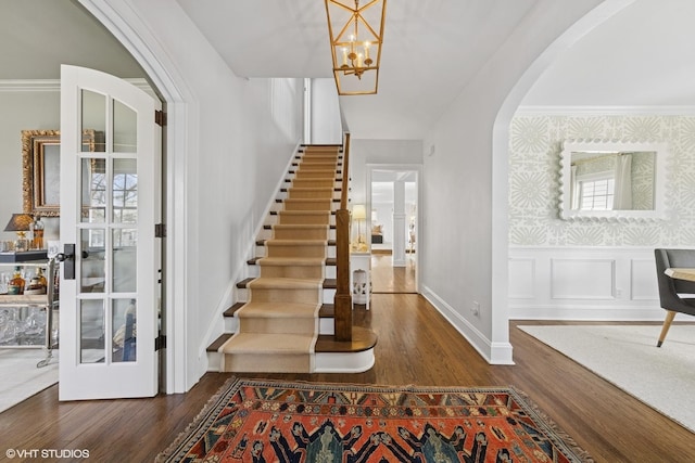 foyer entrance with wallpapered walls, wood finished floors, arched walkways, and wainscoting