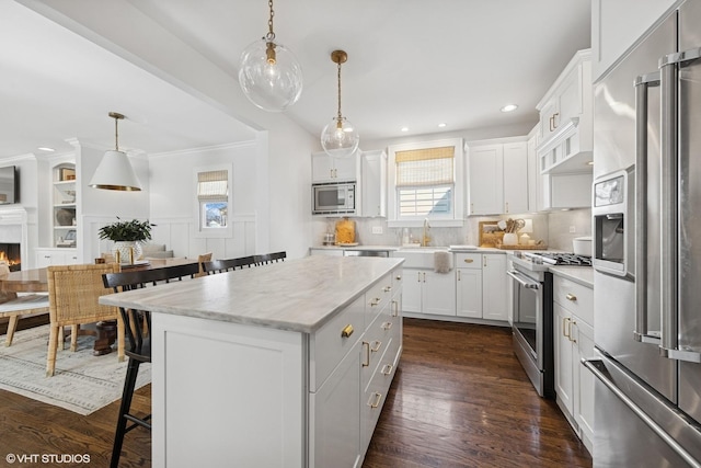 kitchen featuring a kitchen island, a breakfast bar, a lit fireplace, a sink, and appliances with stainless steel finishes