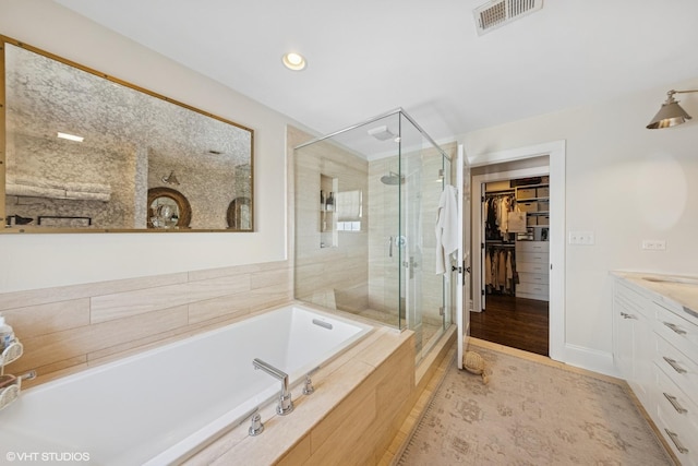 full bath featuring a spacious closet, visible vents, a garden tub, a stall shower, and vanity