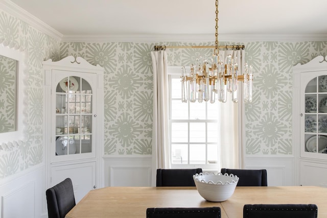 dining space with a wainscoted wall, a notable chandelier, ornamental molding, and wallpapered walls