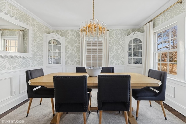 dining space with a wainscoted wall, wallpapered walls, an inviting chandelier, and wood finished floors