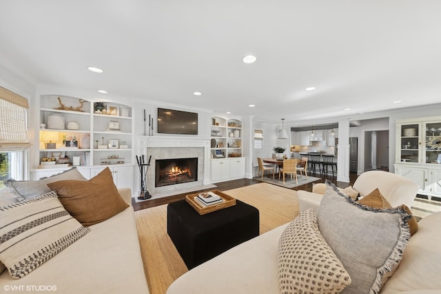 living area featuring built in shelves, wood finished floors, a fireplace, recessed lighting, and crown molding