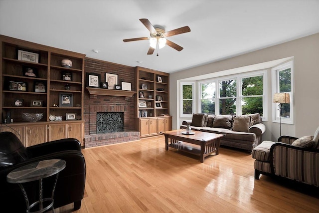 living area featuring built in features, light wood-type flooring, a fireplace, and a ceiling fan